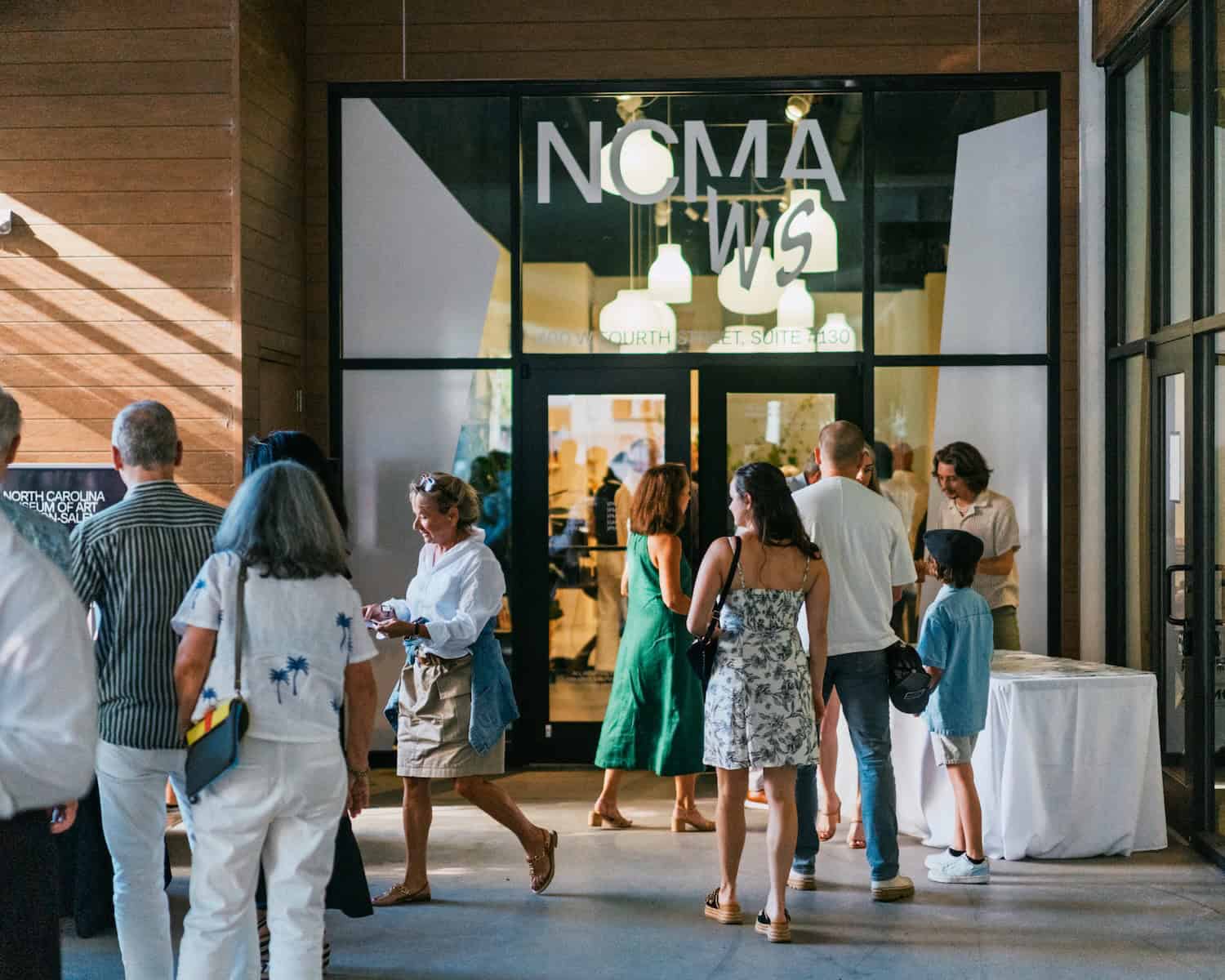 Visitors gather outside the glass-walled entrace to a gallery space.