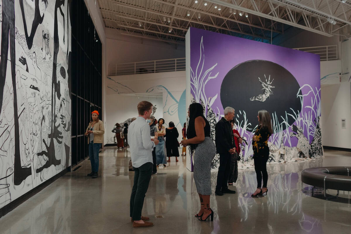 A group of people talk and examine tall, colorful murals in an open gallery space.